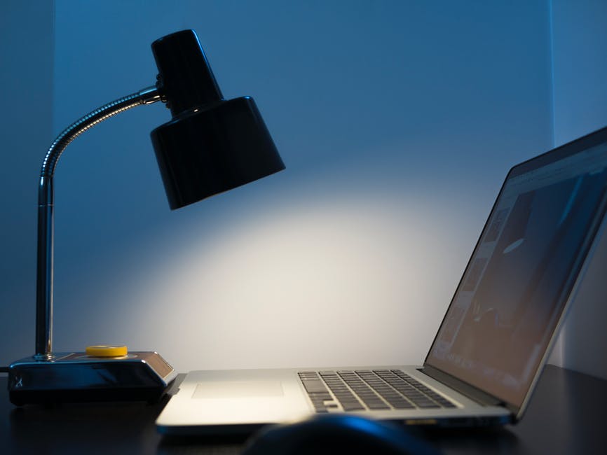 A desk lamp shining onto a laptop in a dark room