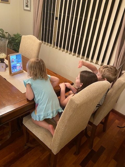 Group of three young children sit on sofa and look at screen in front of them 