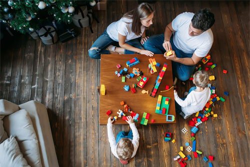 Aerial shot of two children and their parents playing with Lego on a wooden table.