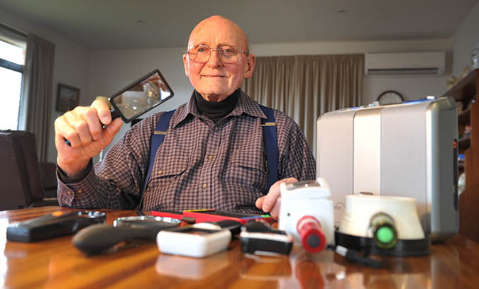 A man holding a magnifier with other items if assistive technology on the table.