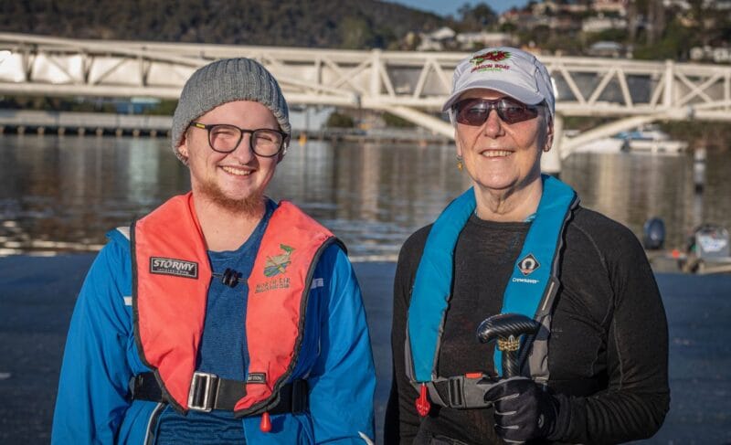 Elliot (left) and Kathy (right) wearing bright coloured life vests and standing beside the river.