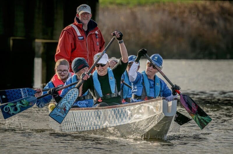 The dragon boat team paddling together, with Kathy at the front left and Elliot on the back left.