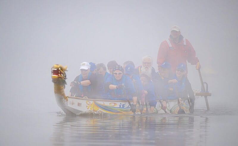A dragon boat surrounded by fog paddling down a river