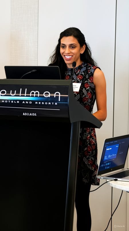 Vithya Vijayakumare stands at a podium to present at the Round Table on Information Access for People with Print Disabilities Conference